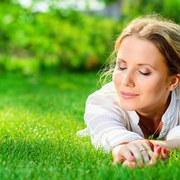 Close-up portrait of a beautiful smiling woman lying on a grass outdoor. She is absolutely happy. 
